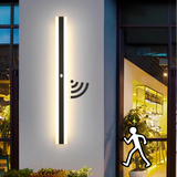 Minimalist black outdoor long LED wall light with motion sensor mounted beside a modern front doo
