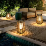 Bohemian rattan outdoor lantern glowing beside a wooden patio table and garden seating