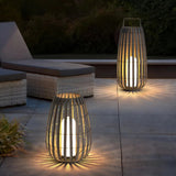 Two woven rattan outdoor floor lanterns casting warm light beside garden sun loungers