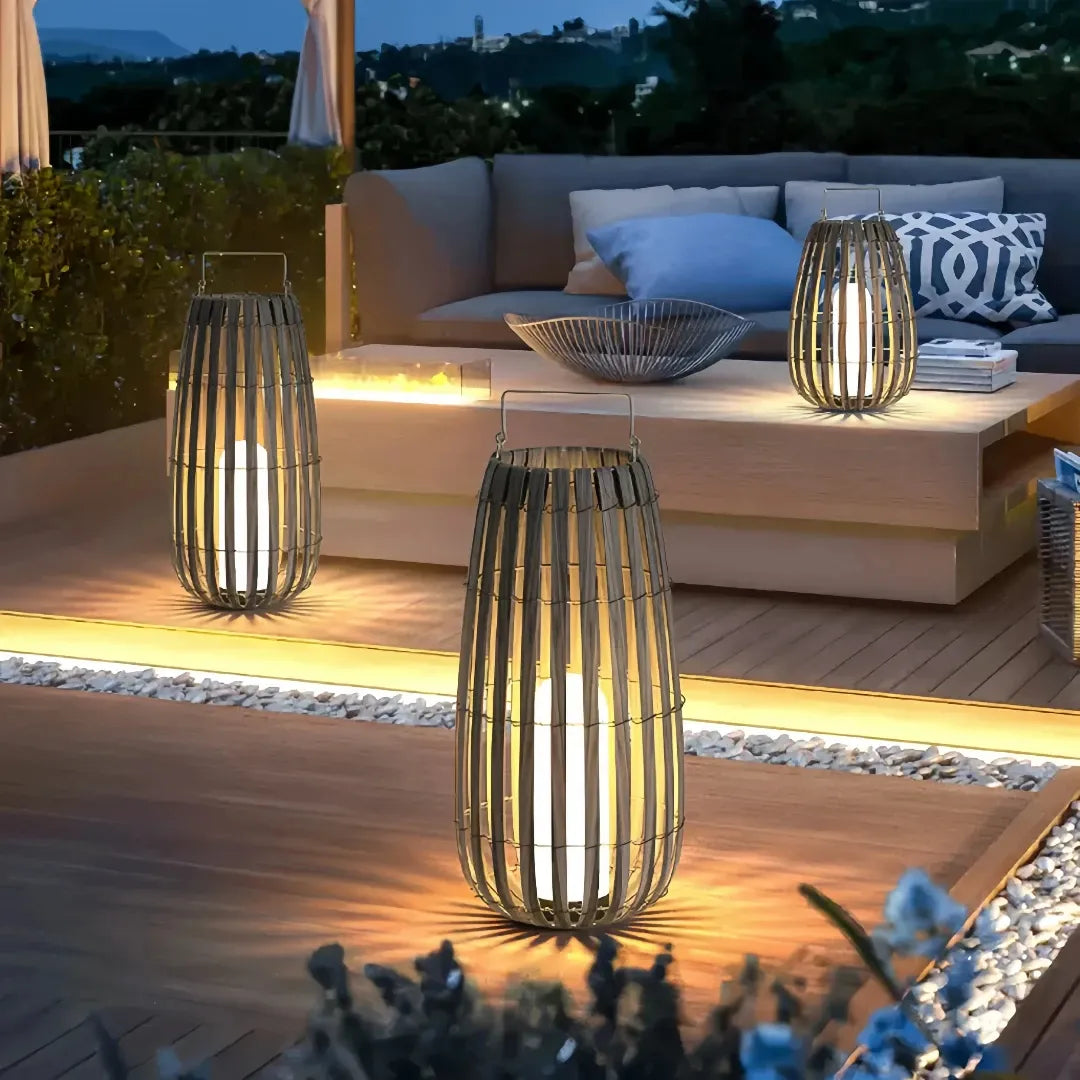 Three boho rattan LED floor lanterns illuminating a modern outdoor patio seating area