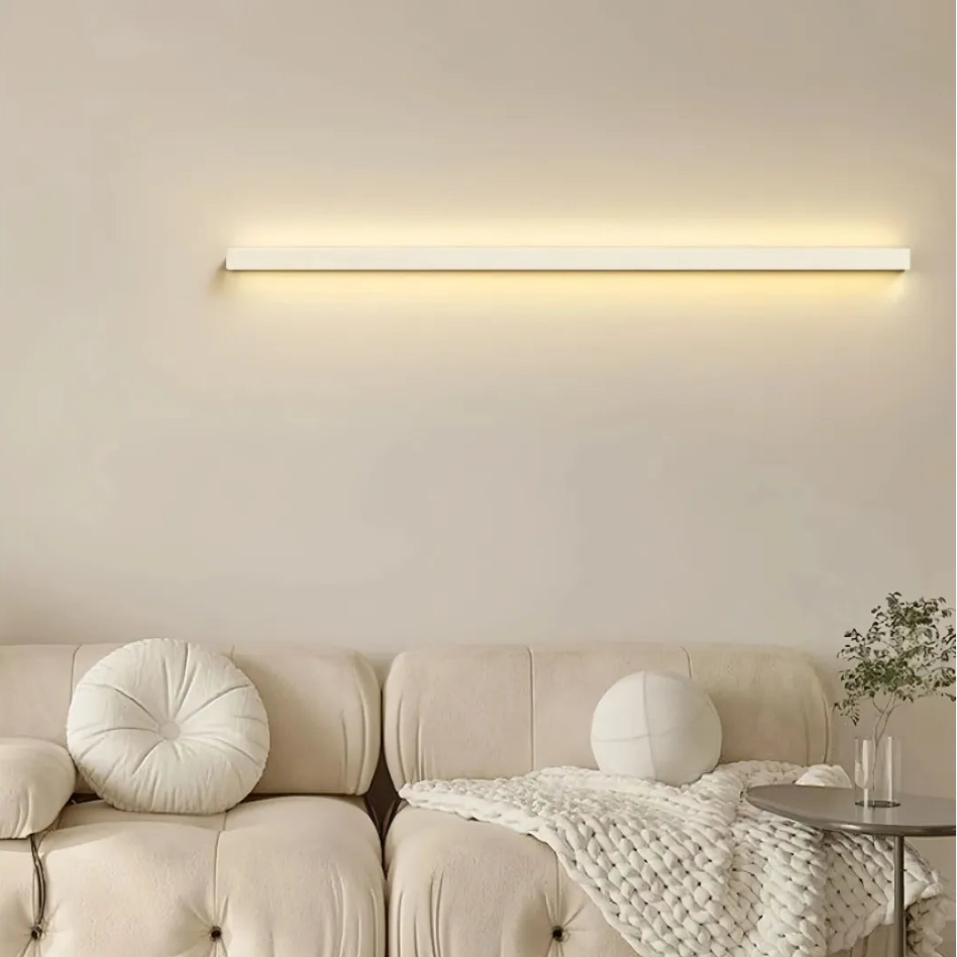 White linear LED wall light mounted horizontally above a sofa