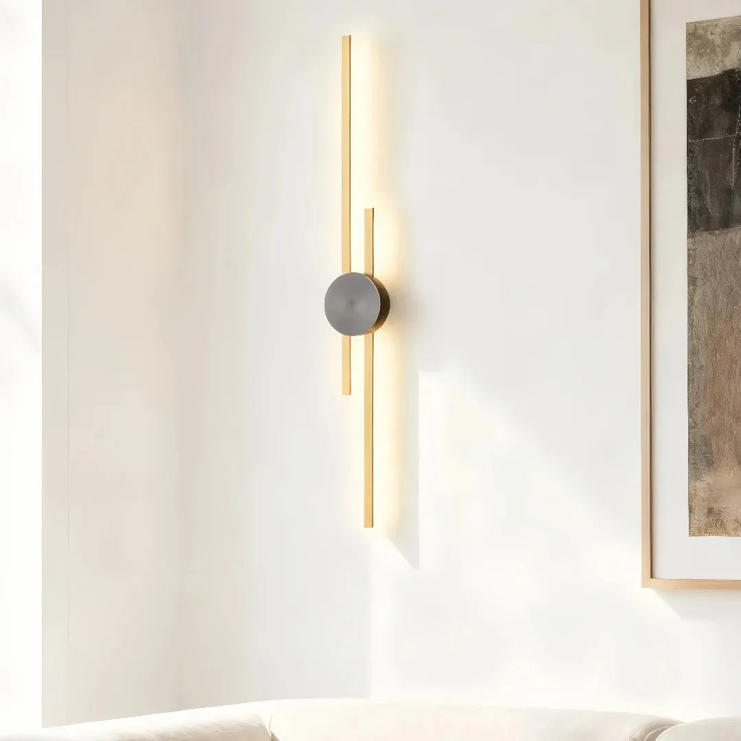 Gold two-line linear LED wall light with a dark centre mount beside framed wall art