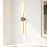 Gold two-line linear LED wall light with a dark centre mount beside framed wall art