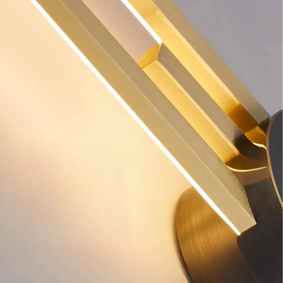 Gold two-line linear LED wall light with a dark centre mount beside framed wall art