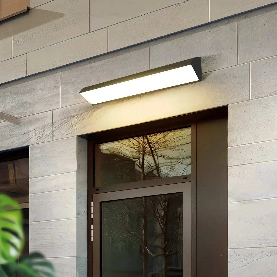Linear LED wall light above a door on a stone-clad exterior wall