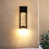 Black crystal glass wall light illuminating an exterior wall beside a patio seating area