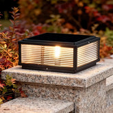 Modern black solar garden pillar light with clear glass shade on a stone wall