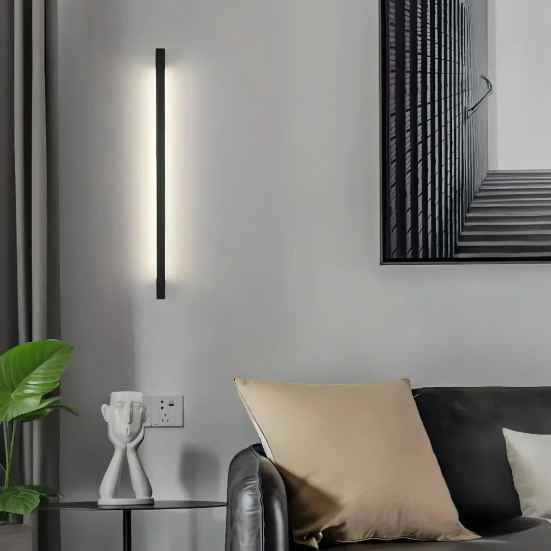Slim black LED wall light installed vertically beside a sofa