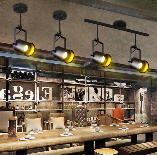 Industrial-style black track spotlights illuminate a rustic café interior, highlighting wood tables and metal shelving for a warm, modern ambiance.