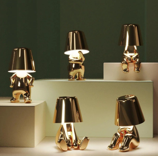 Gold figurine table lamps with playful human forms, metallic finish and warm ambient light, modern decorative lighting design by Clowas.
