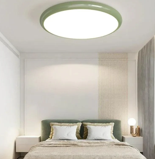 Modern minimalist bedroom with a round LED flush mount ceiling light, soft ambient glow, green headboard and bedside tables, cozy interior lighting.