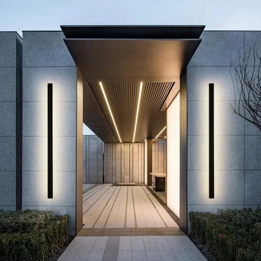 Modern minimalist entrance with grey stone walls, linear outdoor wall lights and ceiling LED strips, softly illuminating the walkway and courtyard.