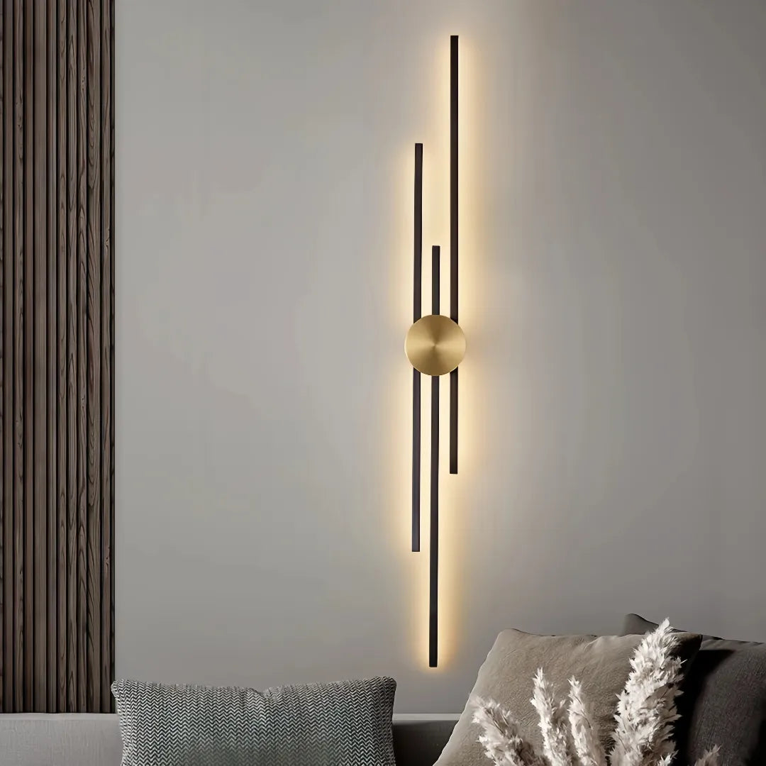 Black three-line linear LED wall light with a gold centre mount beside a television