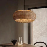 Oval woven rattan pendant light above a dining table with ceramic vases
